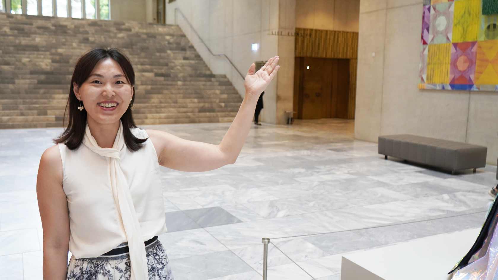 A young woman, Xue Bai, stands in the entrance hall of the Kunsthaus Zürich, gesturing toward a work of art.