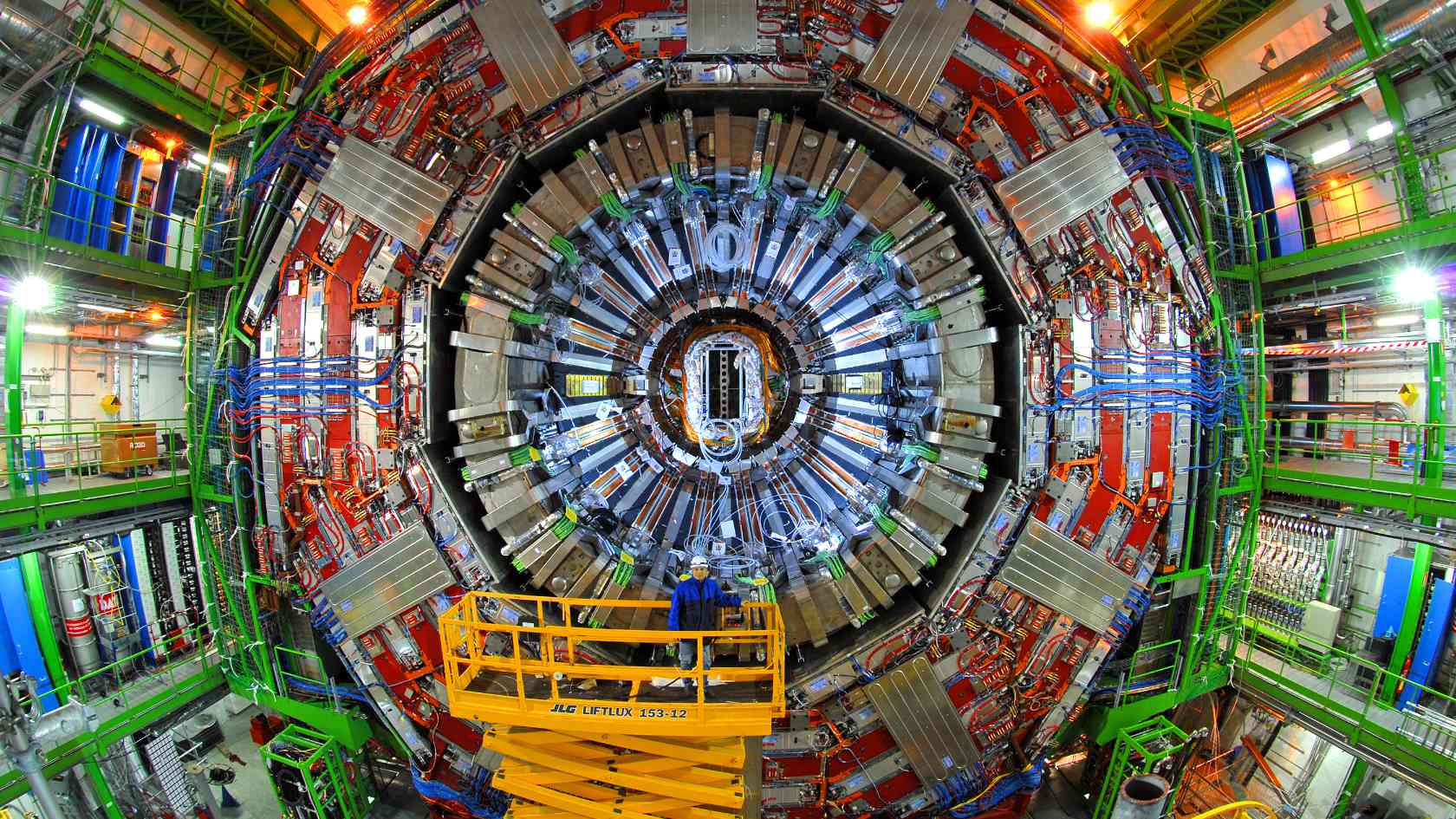 Man standing on a lifting platform in front of the CMS detector of the Large Hadron Collider at CERN.
