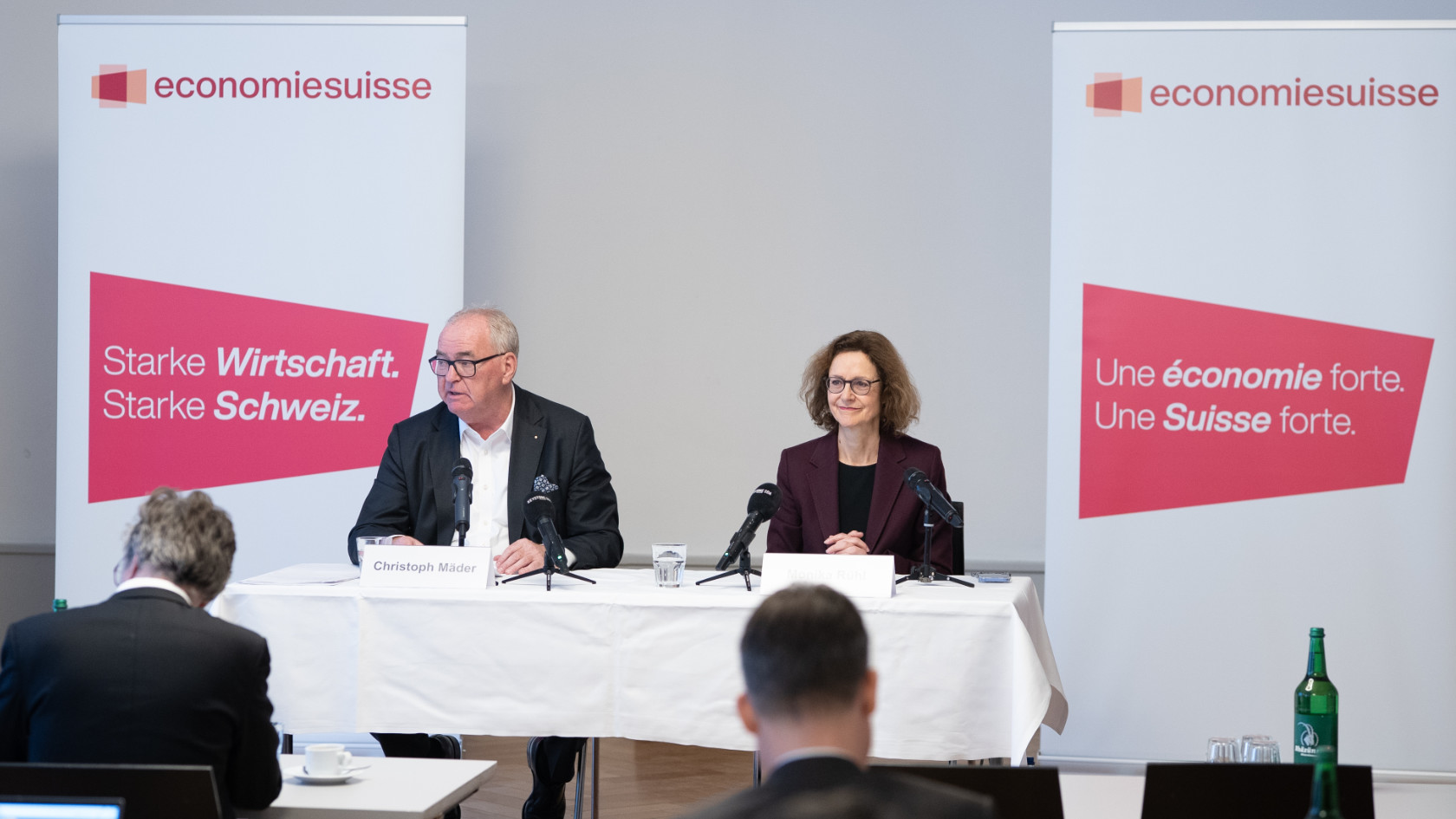 Christoph Mäder und Monika Rühl sitzen an einem Tisch mit Mikrofonen vor zwei Roll-ups mit dem Logo von economiesuisse und Texten in Deutsch und Französisch