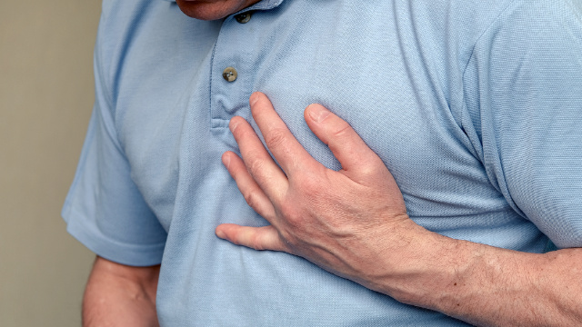The image shows a man in pain holding his left hand to his left chest, symbolizing a possible heart attack.