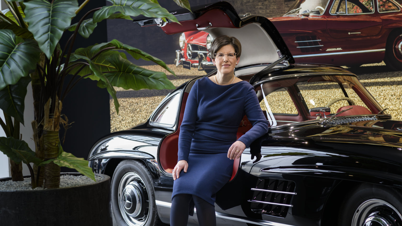 Karin Stüber is sitting in the open door of an old Mercedes coupe.