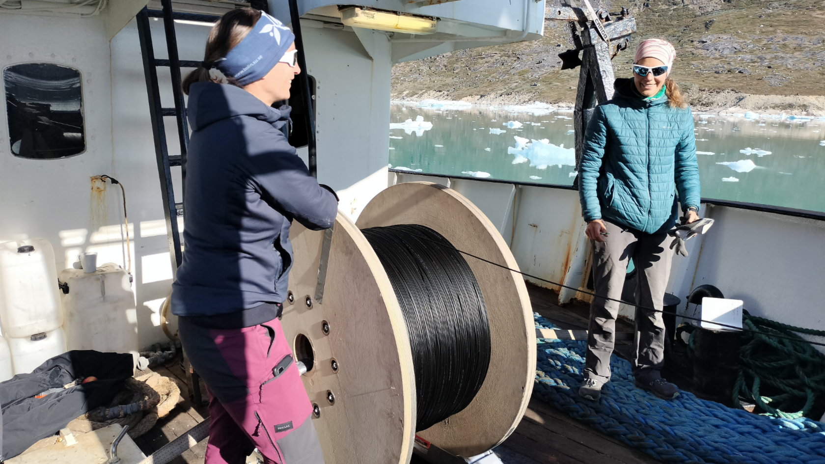 Two researchers lower the fiber optic cable from the reel to the sea floor to take measurements.