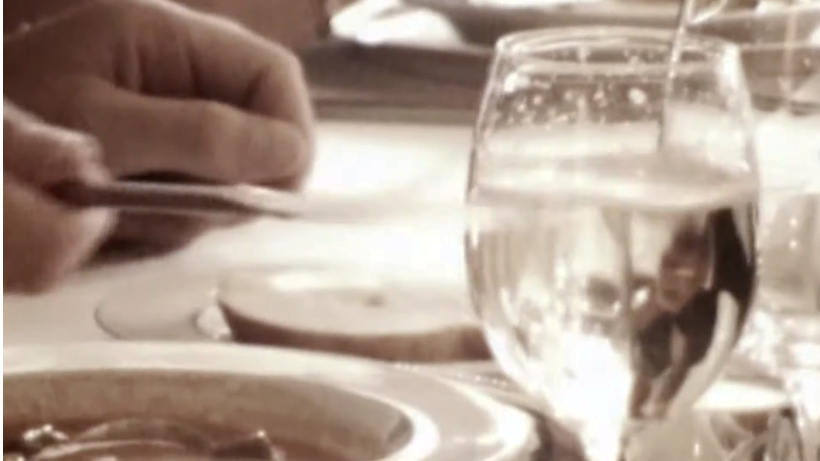 A hand holding a knife knocking on a glass in preparation for a speech at a banquet, film still from "Festen" from 1998